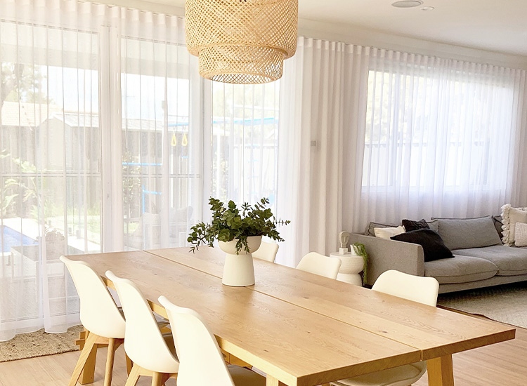 Fresh, coastal style open plan living and dining room featuring white sheer curtains along the windows and sliding doors. 