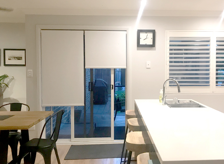 Open plan kitchen-dining room with plantation shutters and roller blinds over the sliding door. 