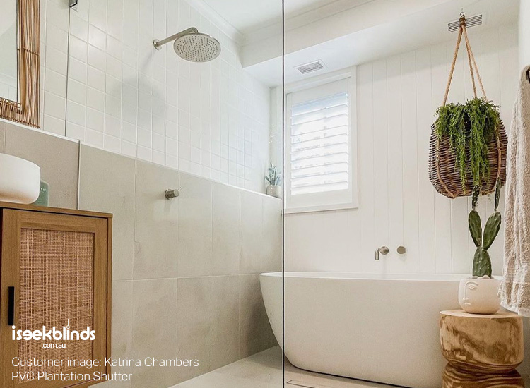 Stunningly renovated, coastal-style bathroom with a free standing bath, rattan timber vanity and white plantation shutter on the window.