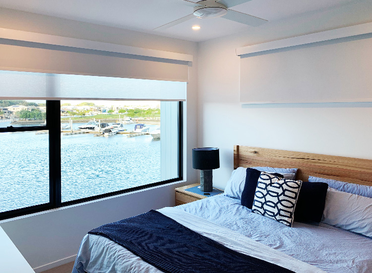 Bedroom with water views and white roller blind and pelmet on the wide window.