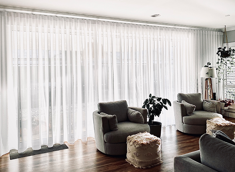 A family living room with modern, comfortable furniture in front of a long wall of beautiful white sheer curtains.