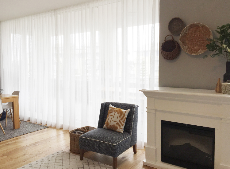 A contemporary apartment with a wall of beautiful white sheer curtains next to an in-built fireplace. 