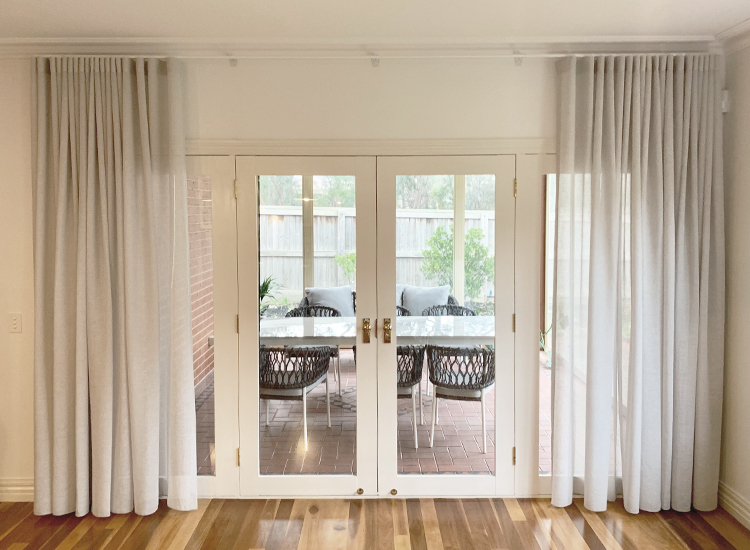 Light grey sheer curtains opening over a set of french doors out to a patio with outdoor furniture.