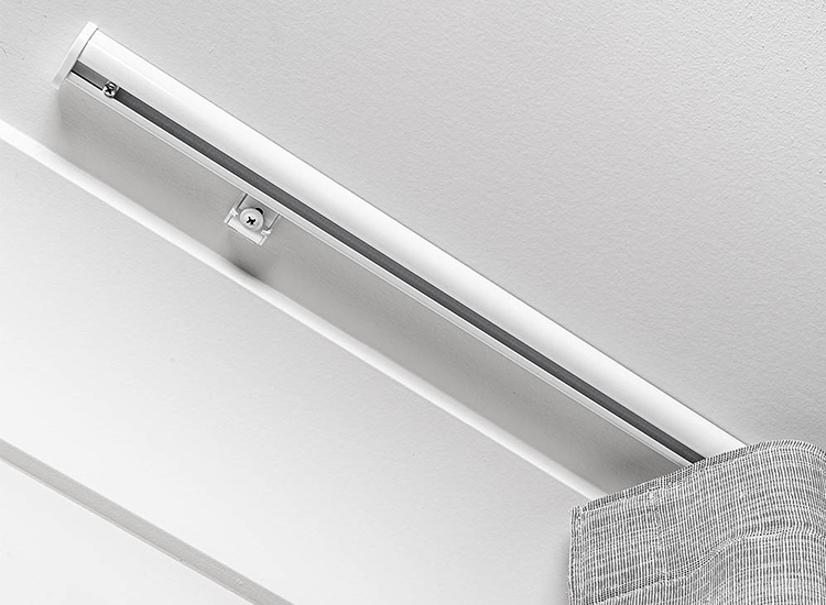 Detail of a white, ceiling mount curtain track with a grey curtain attached, sitting next to a cornice.