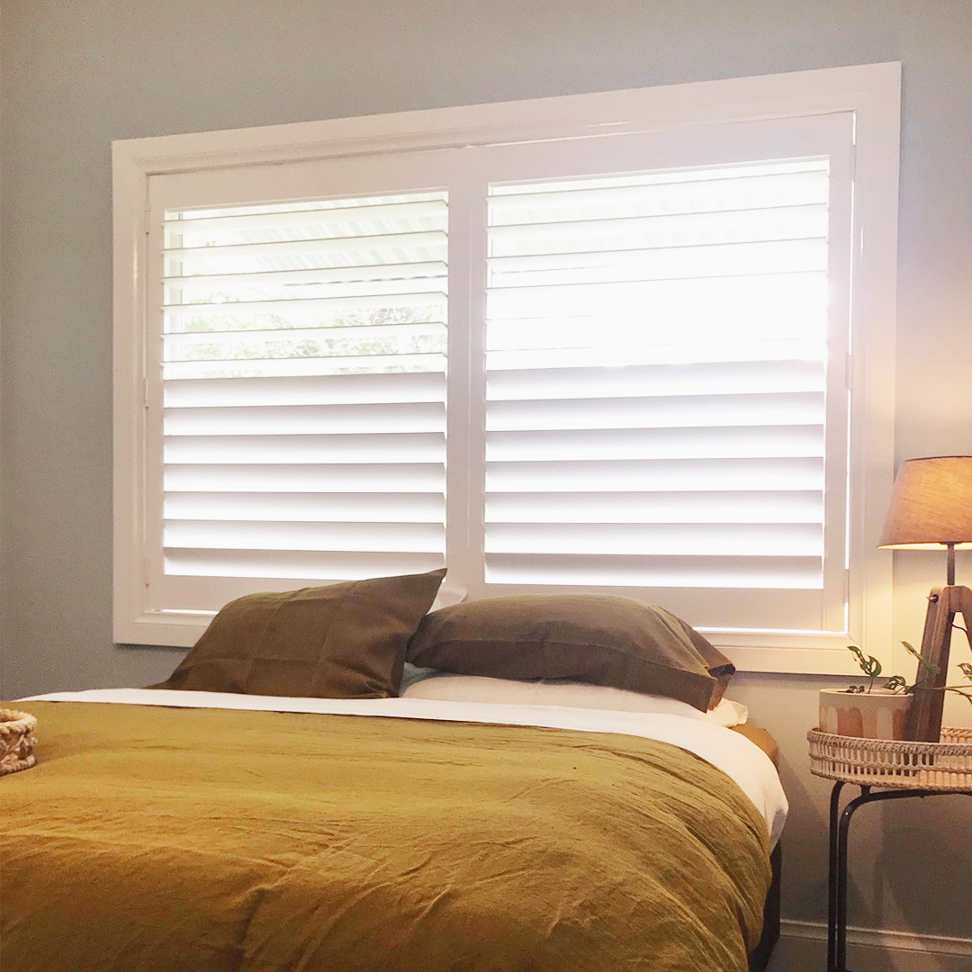 Guest bedroom with grey walls featuring a white plantation shutter above the bed. 