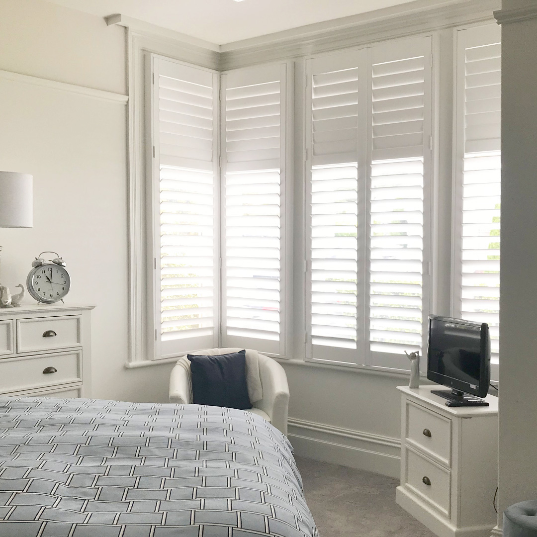 Traditional style bedroom interior featuring white plantation shutters on a corner window