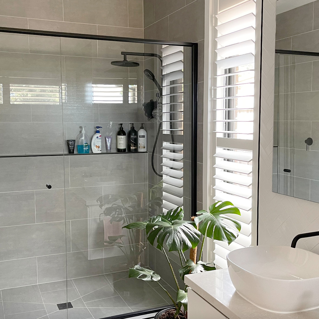 Modern bathroom featuring a walk-in shower with black taps and a white plantation shutter on a tall narrow window