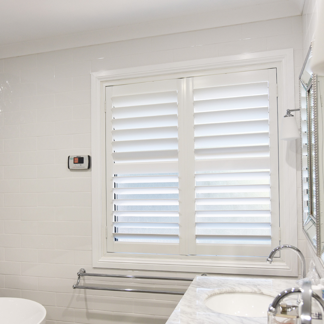 Renovated white and grey bathroom, with a white plantation shutter next to a marble vanity. 