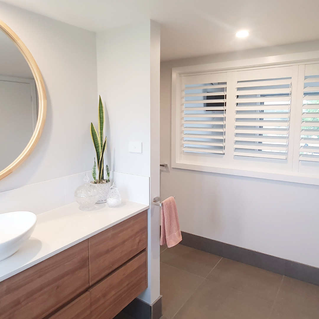 White bathroom with timber vanity and white plantation shutter