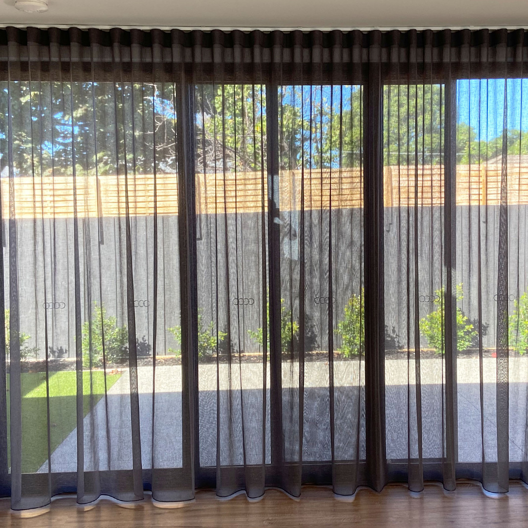 Bedroom with dark grey sheer curtains and blockout roller blinds behind, looking out to a courtyard. 