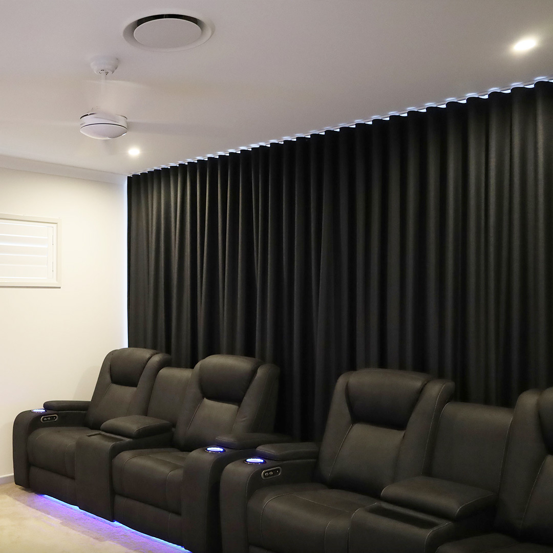 Home theatre room featuring cinema chairs and black blockout curtains behind.