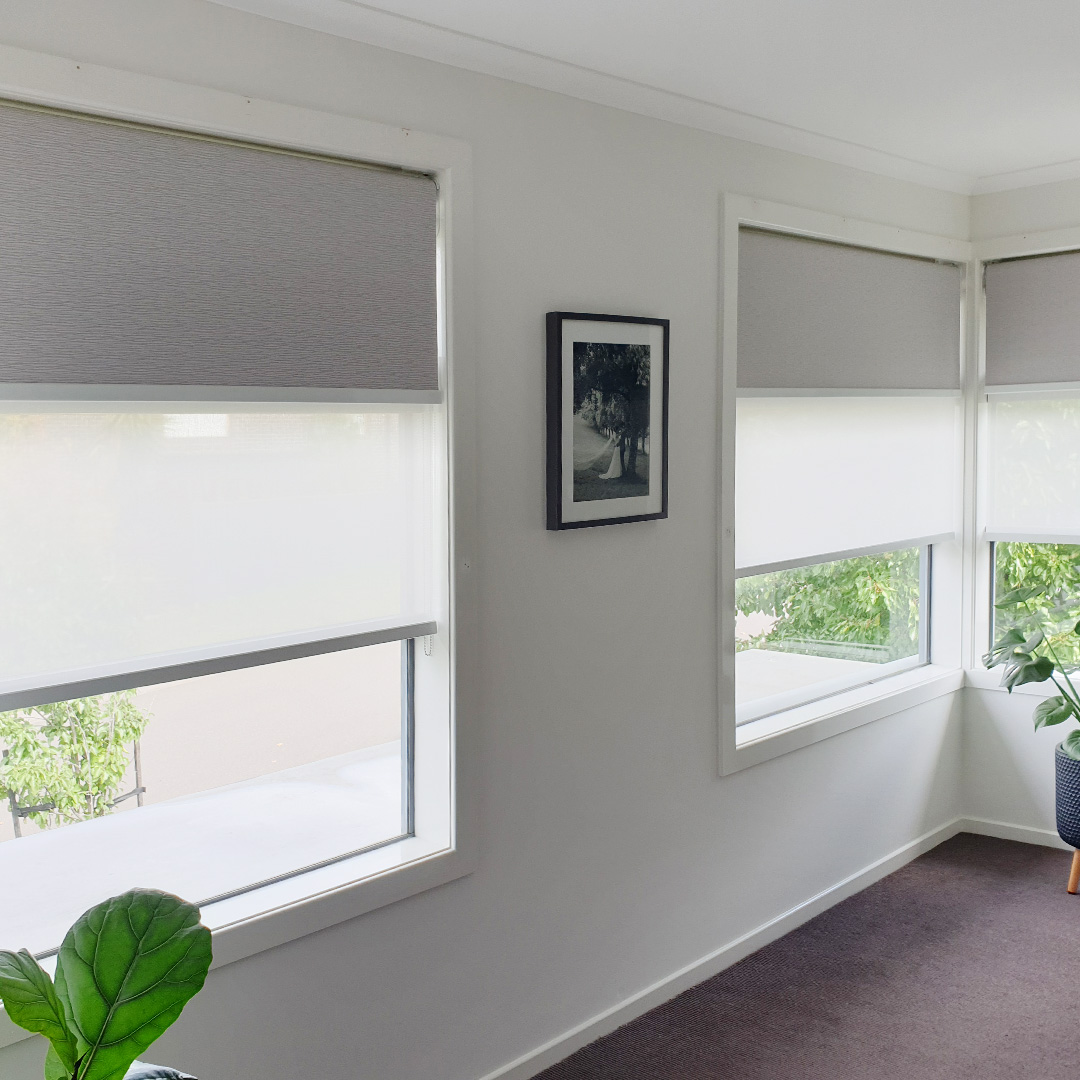 Double motorised roller blinds on a corner window in a walk-in robe. Blockout blind is light grey, sunscreen blind is white. 