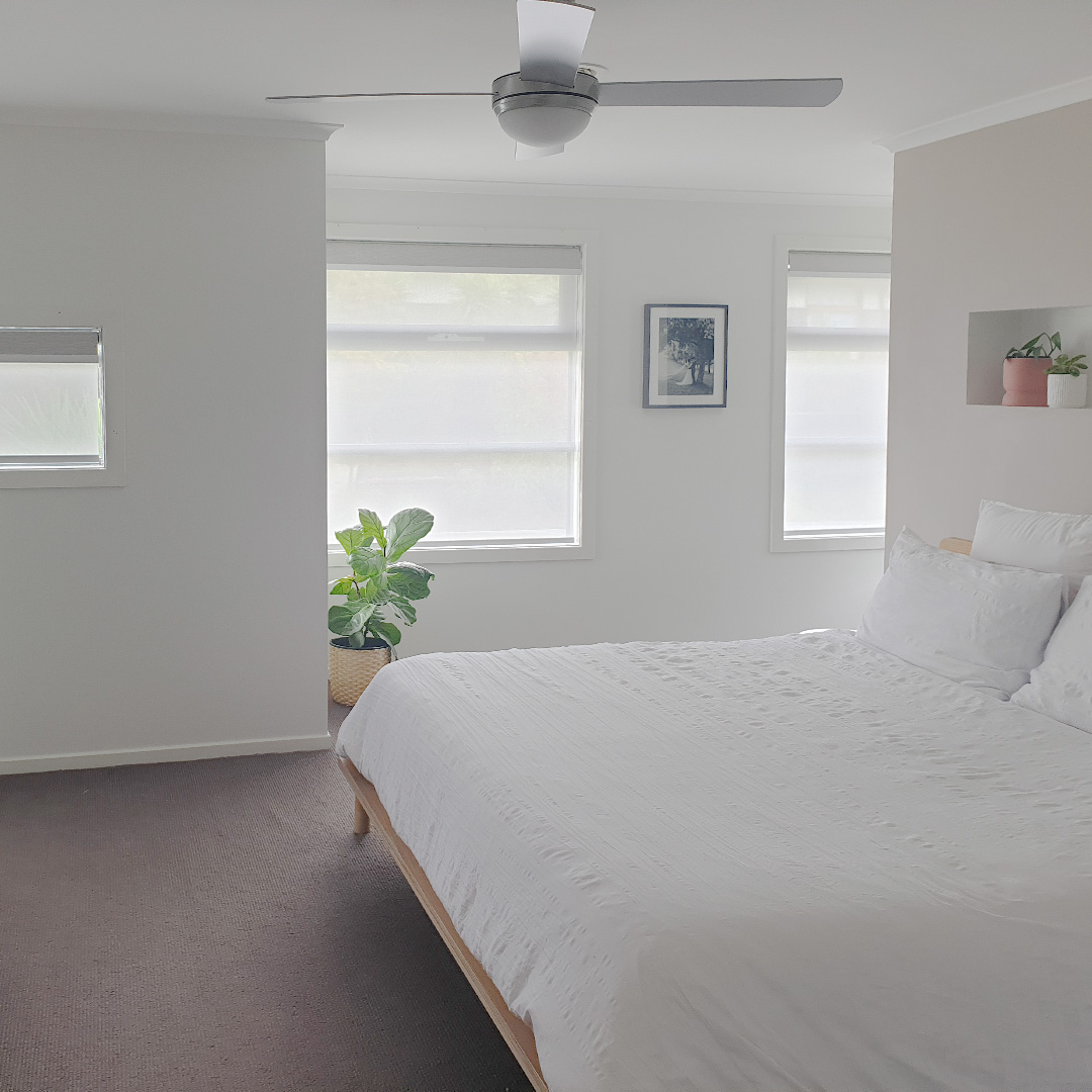 Double motorised roller blinds on three windows in a beautiful bedroom. Blockout blind is light grey, sunscreen blind is white. 