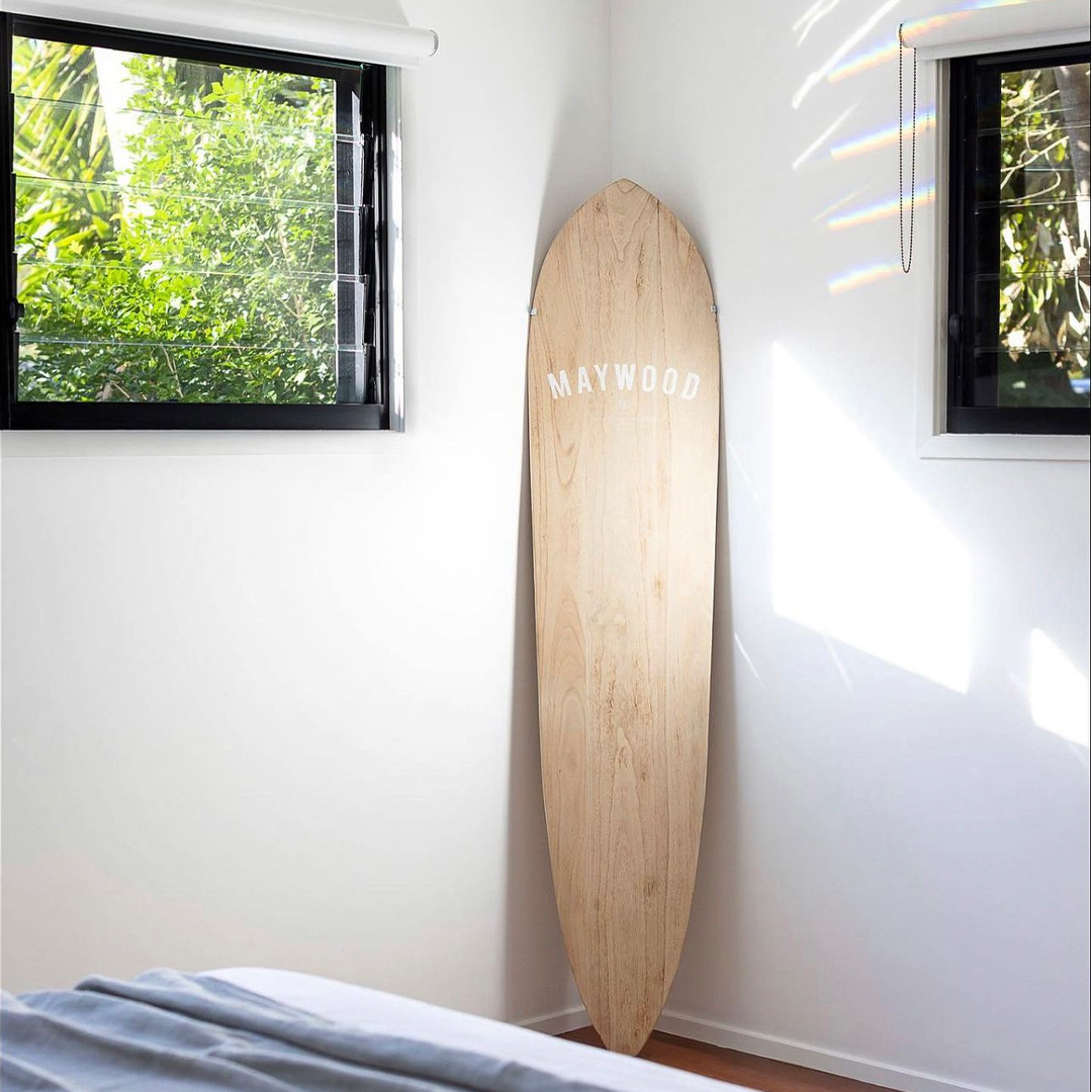 White blockout roller blinds, rolled up to the top in a coastal bedroom with a surfboard in the corner.