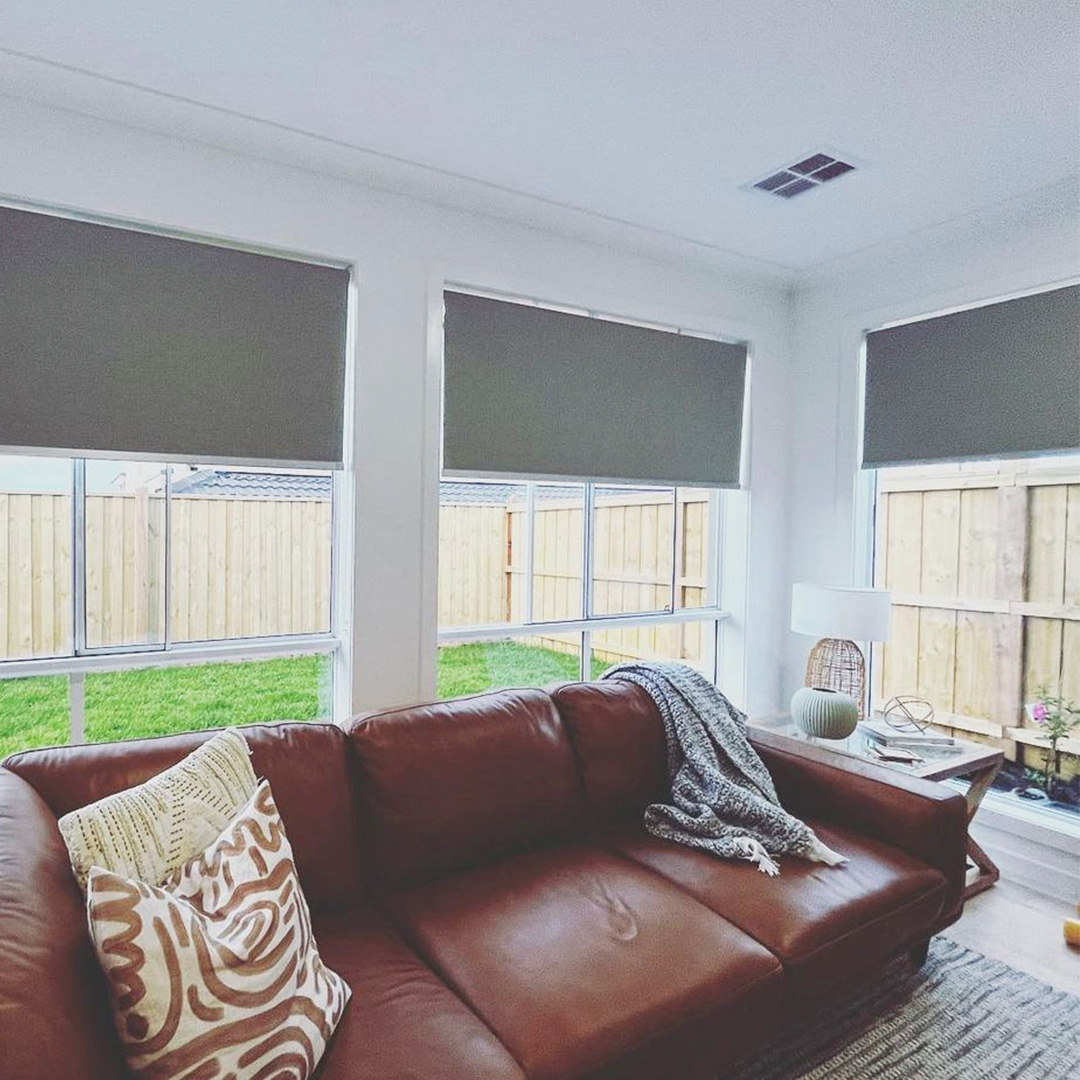 Grey motorised blockout roller blinds in a casual living room with a view of the backyard.