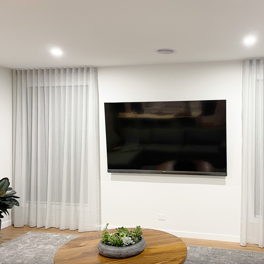 Light grey sheer curtains on narrow windows either side of a television in a bright modern home.