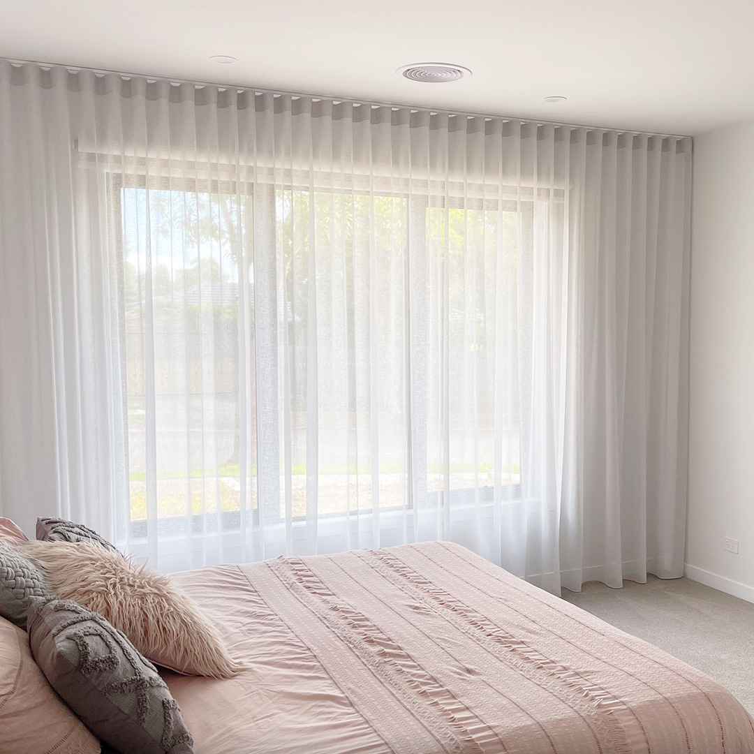 Main bedroom with light grey sheer curtains running from wall to wall and floor to ceiling with lots of natural light. 