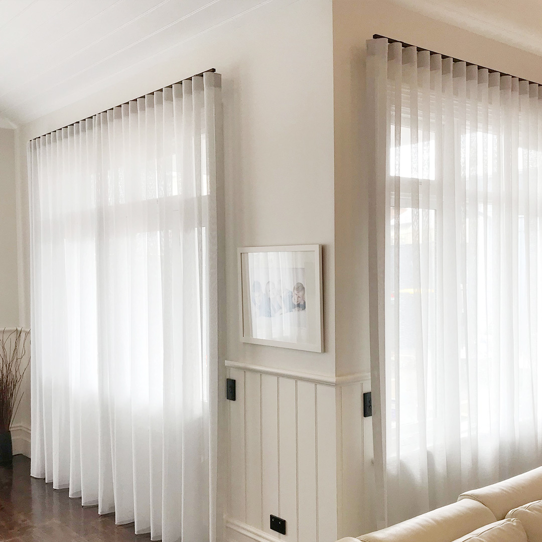 Light grey sheer curtains with black tracks, on two windows of a heritage home. 