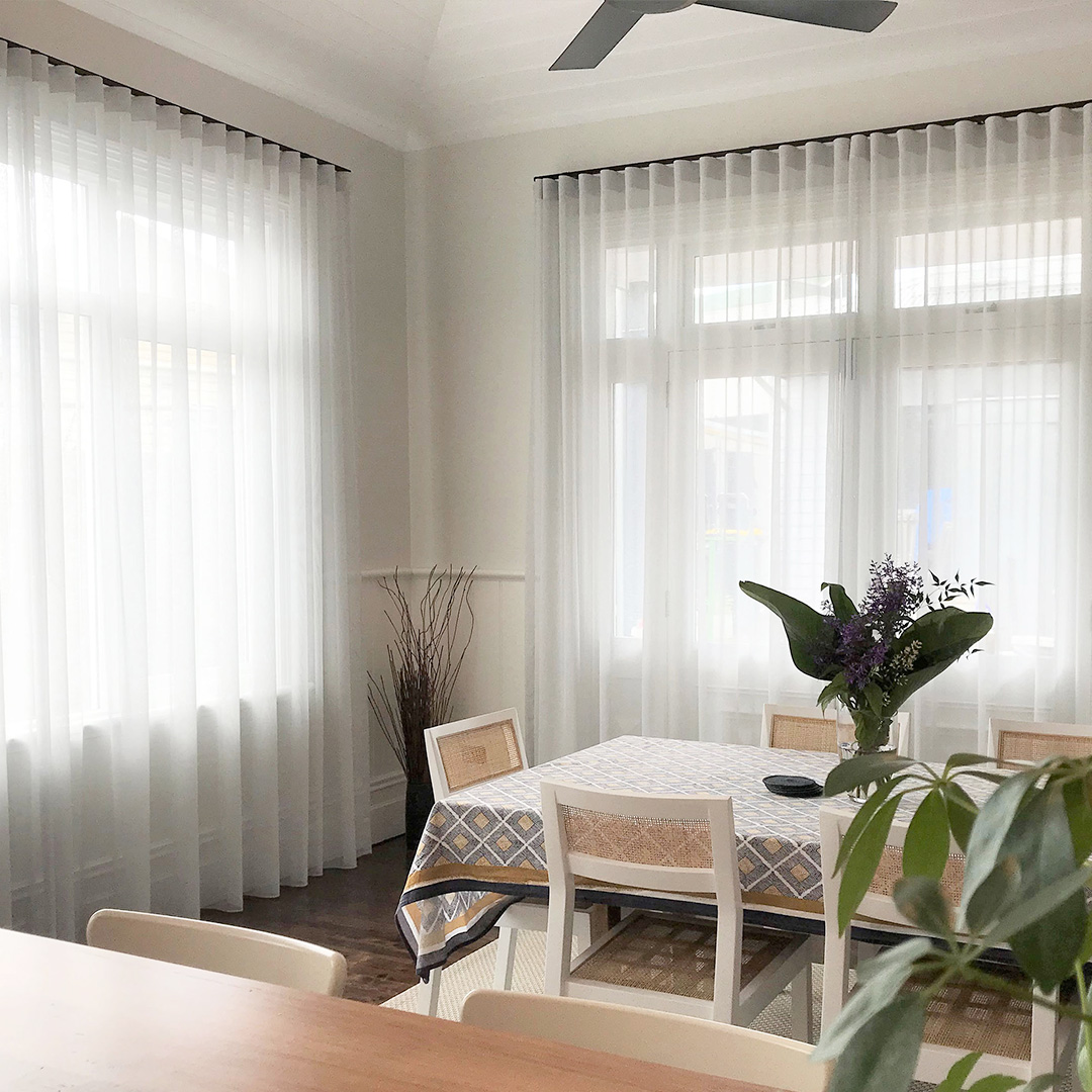 Light grey sheer curtains with black tracks, on two windows of a heritage dining room. 