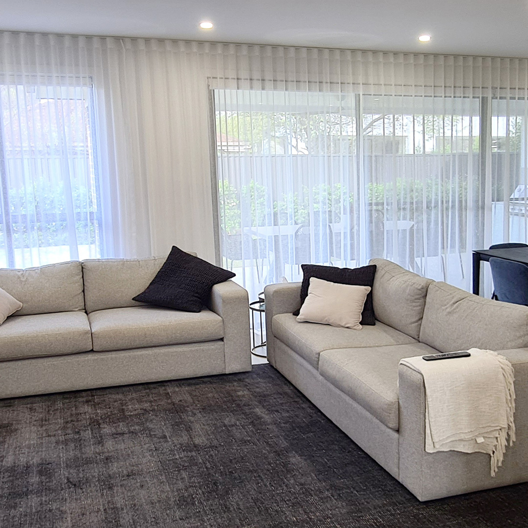 A modern living room neutral sofas and white sheer curtains running the full length of the wall. 