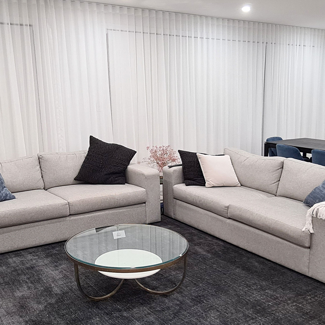 A modern living room neutral sofas and white sheer curtains with blockout roller blinds behind them. 
