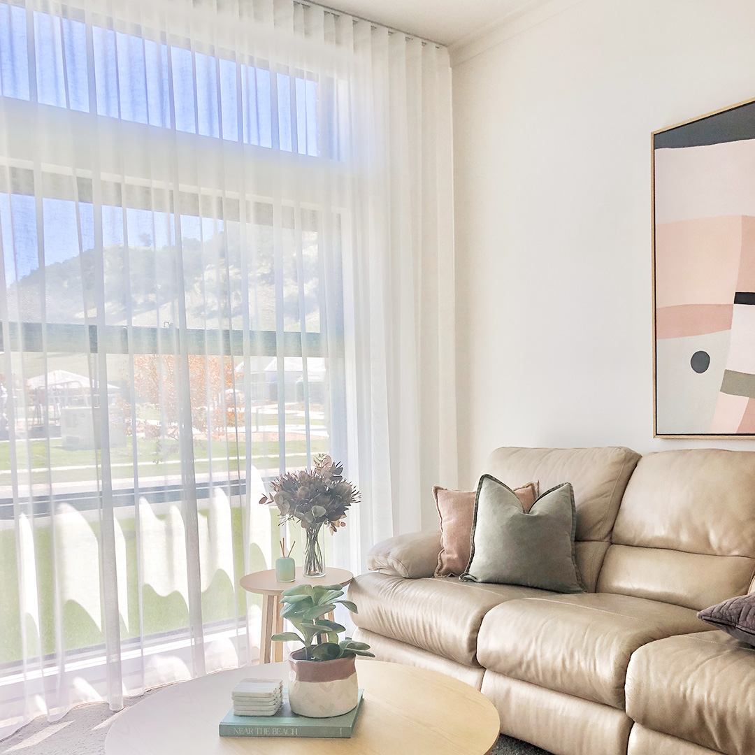 A light and bright living room corner showing the white sheer curtains on the window, with motorised roller blinds behind. 