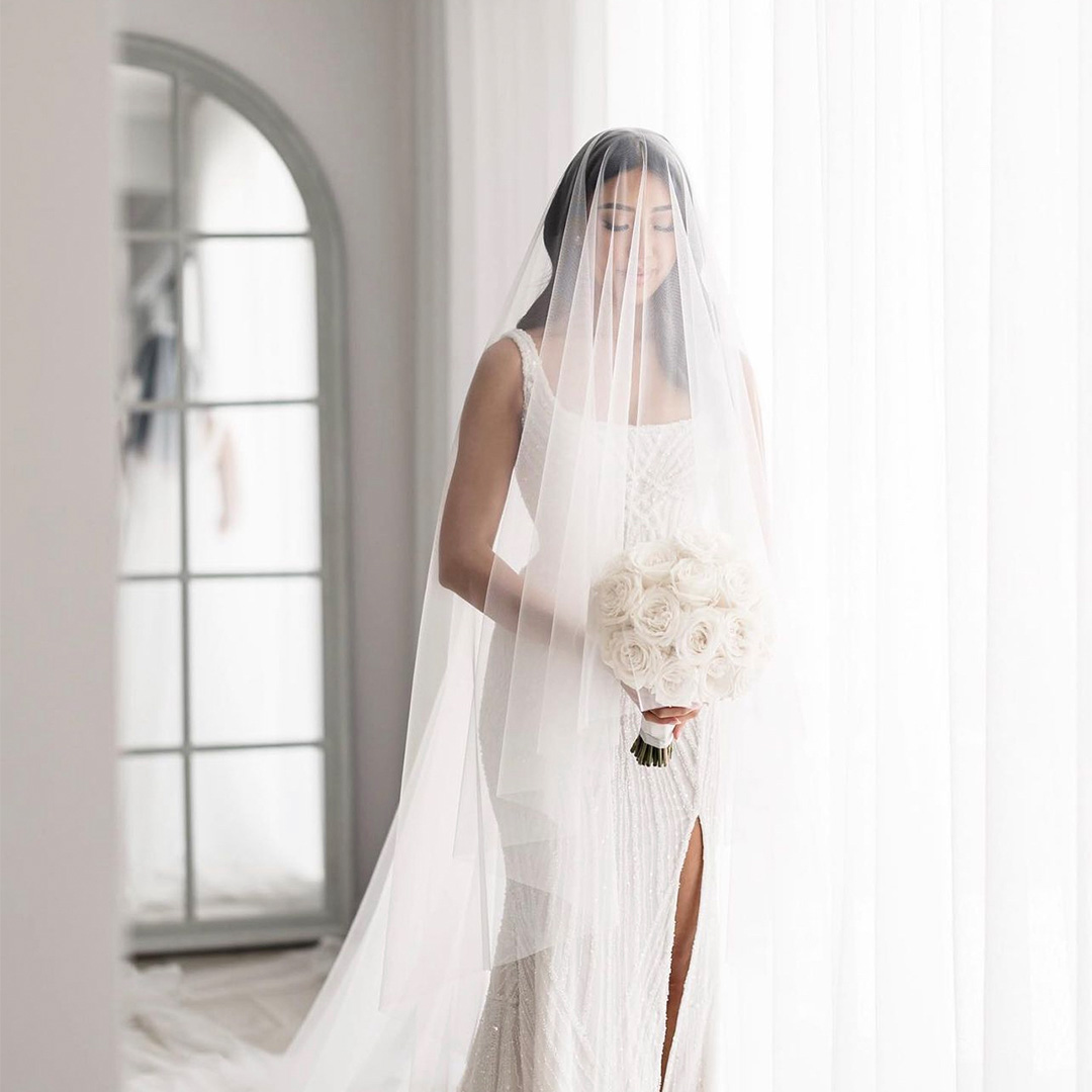 Beautiful bride standing beside a wall of white sheer curtains.