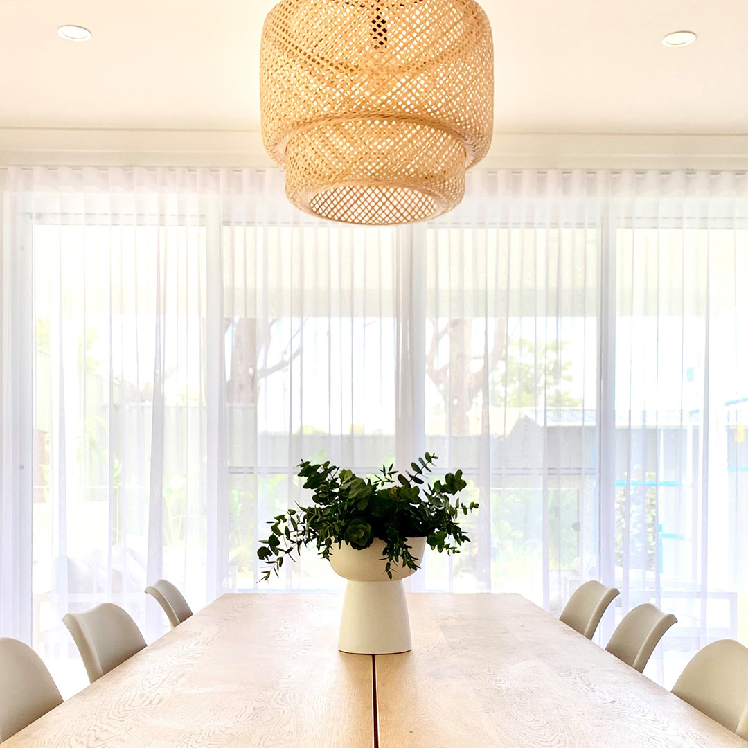 Looking across a coastal dining table to beautiful white sheer curtains with plenty of natural light coming through. 