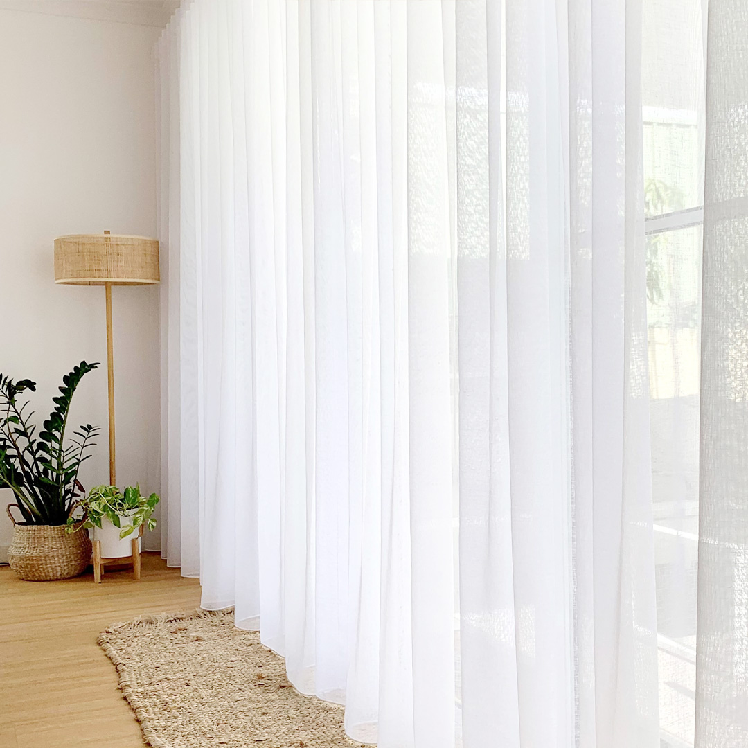 Looking across the face of beautiful white sheer curtains in front of a sliding door. 