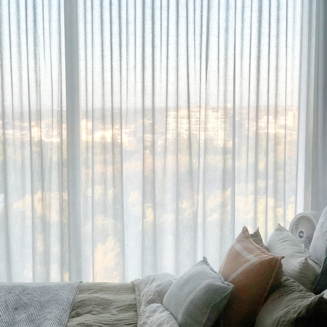 Bedroom with a city view, looking through light grey sheer curtains.  