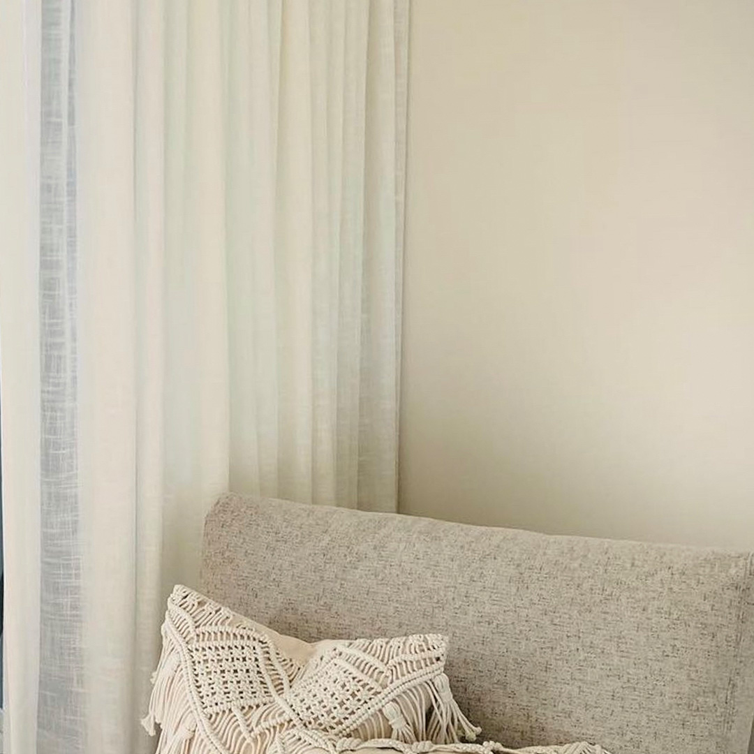 Close up photo of white textured sheer curtains and a bedroom chair. 