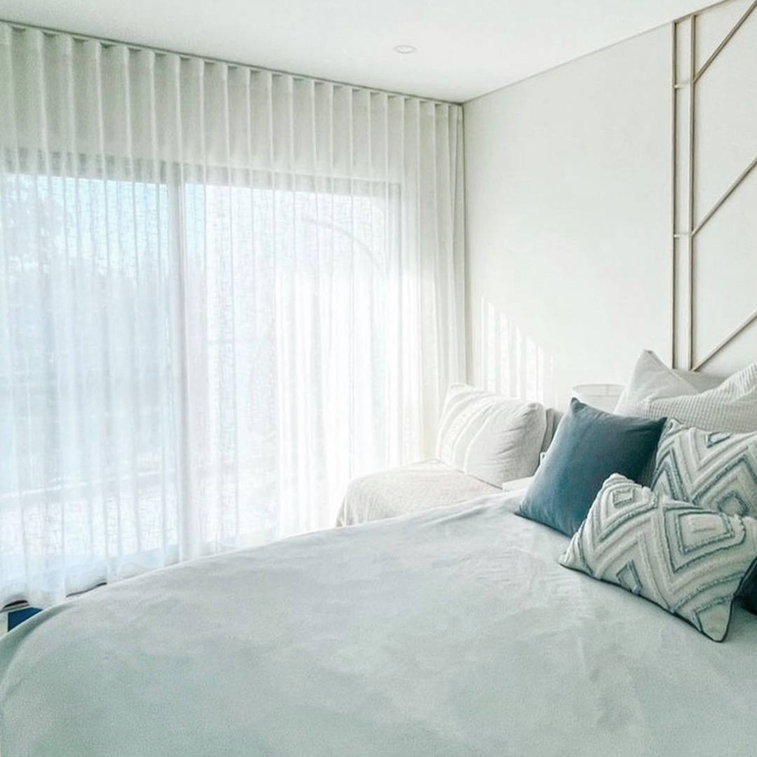 Coastal bedroom in white and blue, showing beautiful white sheer curtains on the window. 