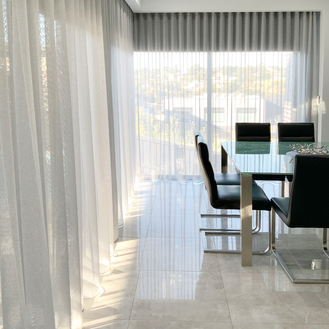 Modern dining room with full length light grey sheer curtains covering the corner window