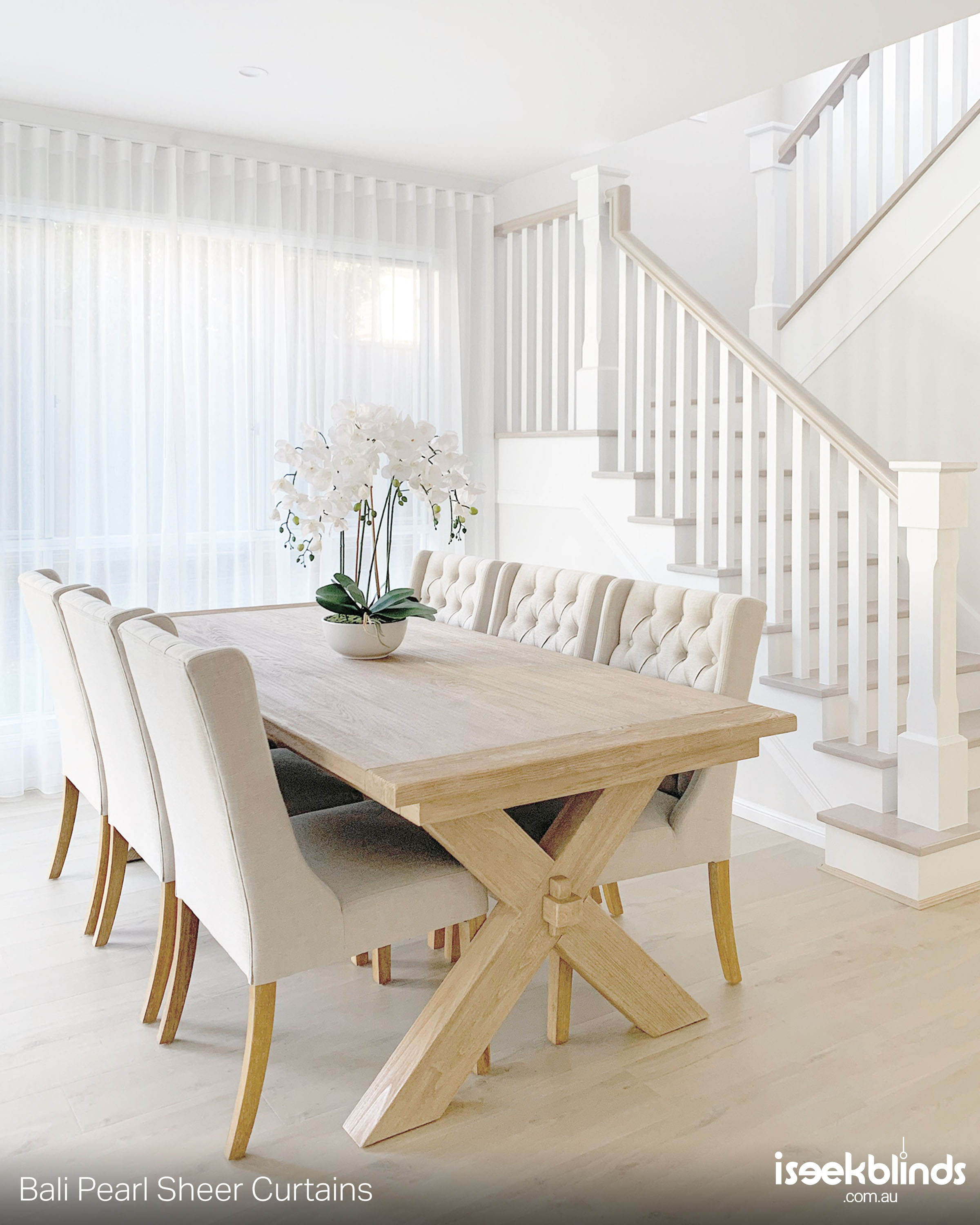 A beautifully styled white dining room with floor to ceiling white sheer curtains on the window. 