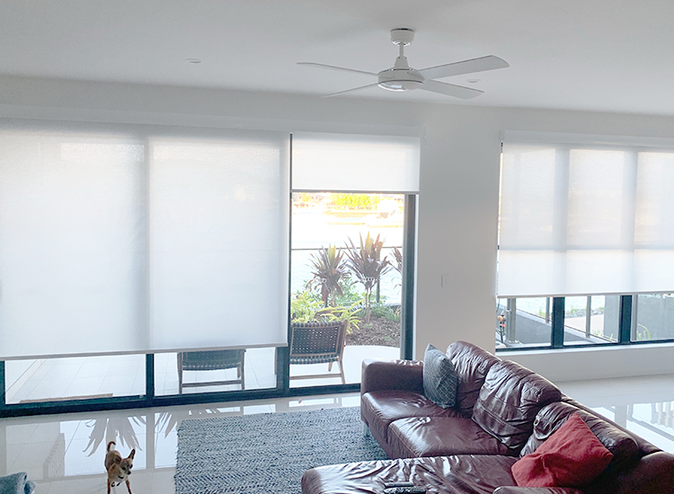 Open plan living space with brown couch and light filter roller blinds on the siding door and window.