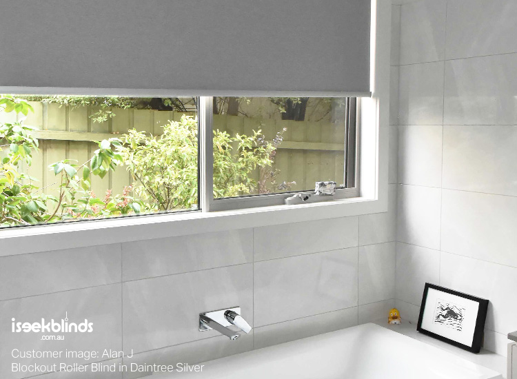 Renovated white and gey bathroom with silver blockout roller blind on the window overlooking the backyard.