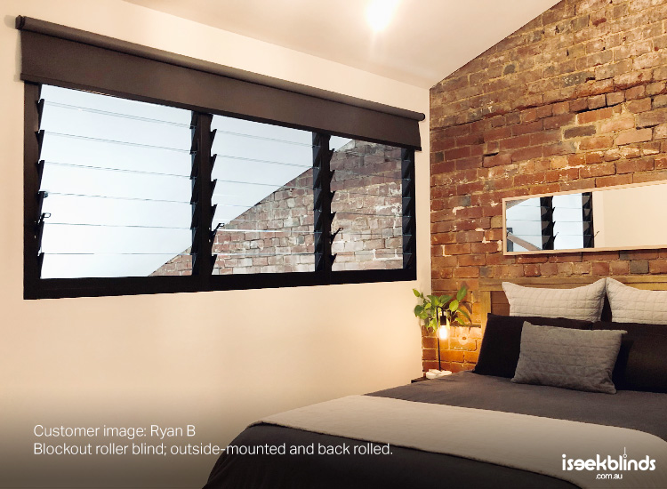 Warehouse conversion bedroom with black roller blind on louvre window.