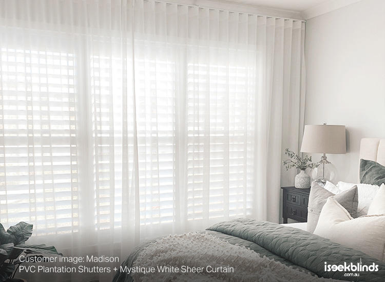 A classic master bedroom featuring plantation shutters behind white sheer curtains.